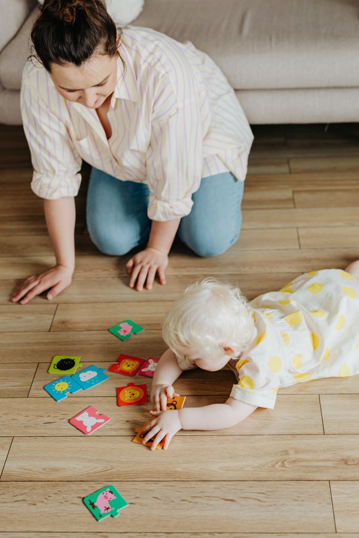 A mother and albino toddler play with colorful flashcards on a wooden floor indoors.